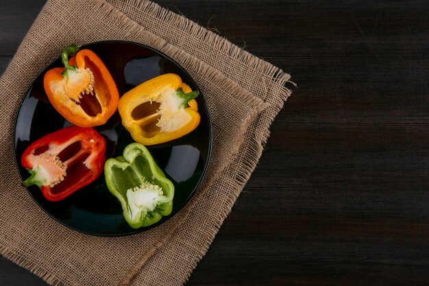 Bovenaanzicht van helften van veelkleurige paprika op een zwarte plaat op een houten oppervlak