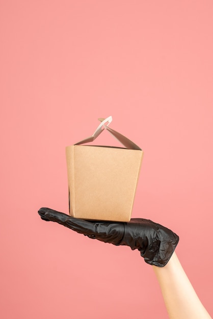 Bovenaanzicht van het dragen van een zwarte handschoenhand met een kleine doos op pastelperzik