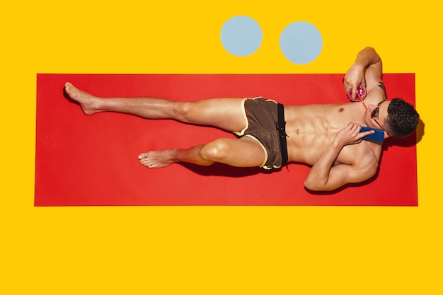 Bovenaanzicht van het jonge blanke mannelijke model rusten op strandresort op rode mat en geel