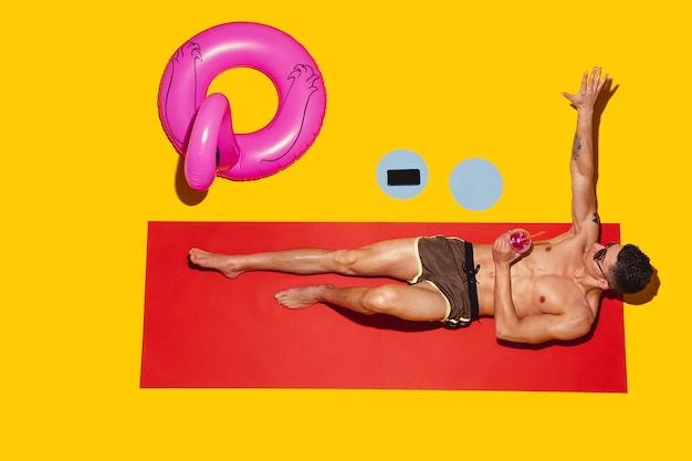 Gratis foto bovenaanzicht van het jonge blanke mannelijke model rusten op strandresort op rode mat en geel