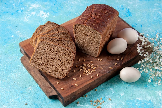 Bovenaanzicht van in tweeën gesneden zwarte sneetjes brood op houten planken bloemeieren op een lichte ijsblauwe achtergrond