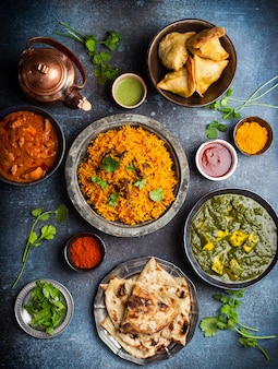Bovenaanzicht van indiase traditionele gerechten en hapjes: kip curry, pilaf, naan brood, samosa's, paneer, chutney op rustieke achtergrond. tafel met keuze uit indiase keuken, diner/buffet