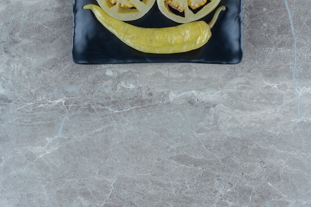 Bovenaanzicht van ingemaakte hete peper op zwarte plaat over grijze achtergrond.