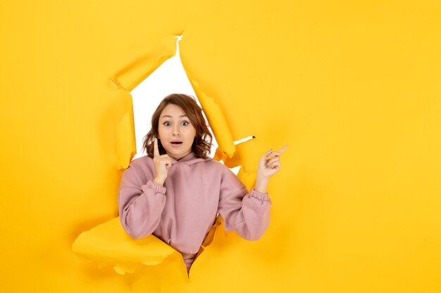 Bovenaanzicht van jonge vrouw die denkt iets te wijzen en vrije ruimte op geel gescheurd