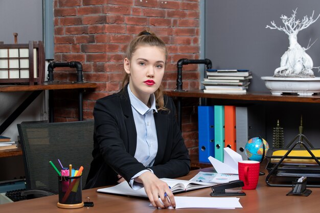 Bovenaanzicht van jonge zelfverzekerde vrouwelijke assistent die aan haar bureau op kantoor zit