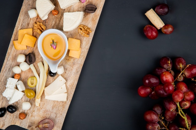 Bovenaanzicht van kaas set met cheddar brie string feta en boter olijfnoten op snijplank met druivenmost en kurk op zwart