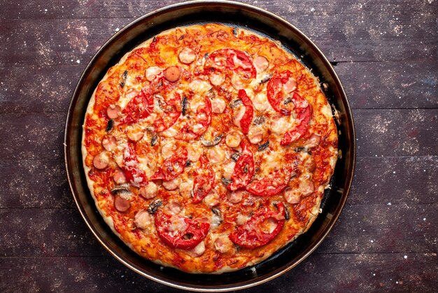 bovenaanzicht van kaasachtige tomatenpizza met olijven en worstjes in de pan op bruin bureau, de kaasworst van het pizzavoedsel