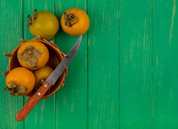 Bovenaanzicht van kaki fruit op een emmer met mes op een groene houten tafel met kopie ruimte