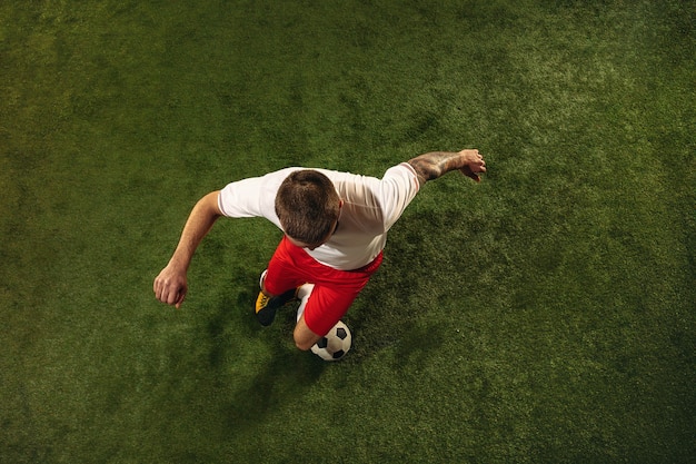 Gratis foto bovenaanzicht van kaukasische voetbal of voetballer op groene achtergrond van gras. jonge mannelijke sportieve model training, oefenen. bal trappen, aanvallen, vangen. concept van sport, competitie, winnen.