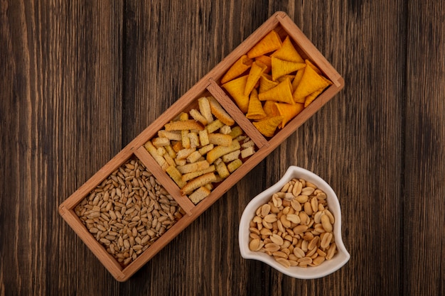 Bovenaanzicht van kegelvorm bugels chips op een houten onderverdeelde plaat met gepelde zonnebloempitten met pijnboompitten op een kom op een houten muur