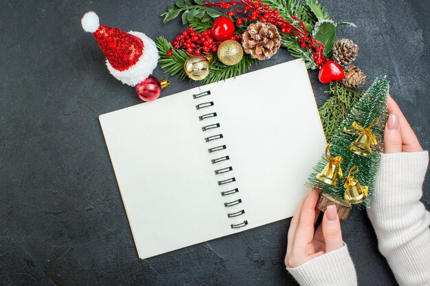 Bovenaanzicht van kerstsfeer met fir takken kerstman hoed hand met kerstboom op donkere achtergrond