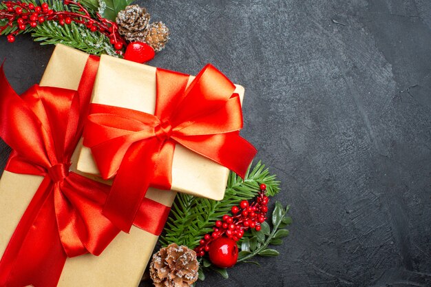Bovenaanzicht van kerstsfeer met mooie cadeaus met strikvormig lint en dennentakken decoratie accessoires aan de rechterkant op een donkere achtergrond