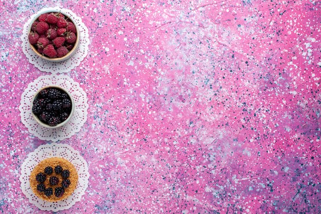 Bovenaanzicht van kleine bramencake met frambozen en verse bramen op het lichtroze oppervlak