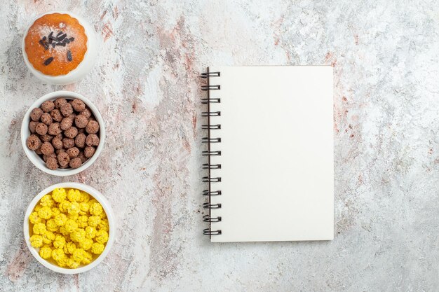 Bovenaanzicht van kleine cake met snoepjes en notitieblok op wit