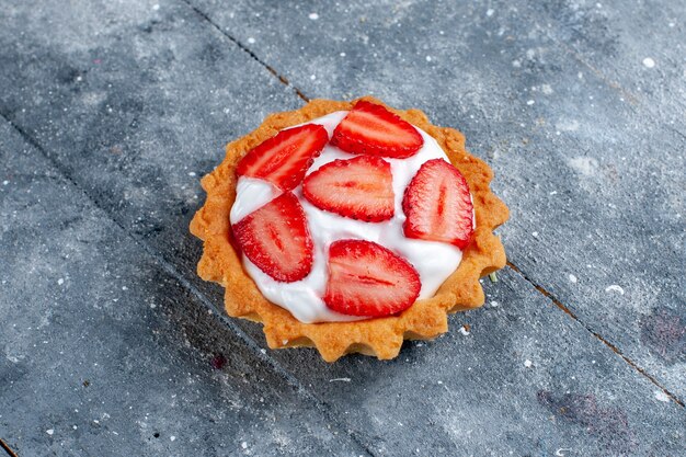 Bovenaanzicht van kleine romige cake met gesneden aardbeien op grijs