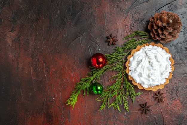 Bovenaanzicht van kleine taart met anijs sterren, twijgen, dennenappel en kerstballen op donkerrood oppervlak