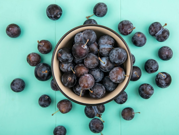 Bovenaanzicht van kleine zure donkerpaarse fruit sleepruimen op een kom op een blauwe achtergrond