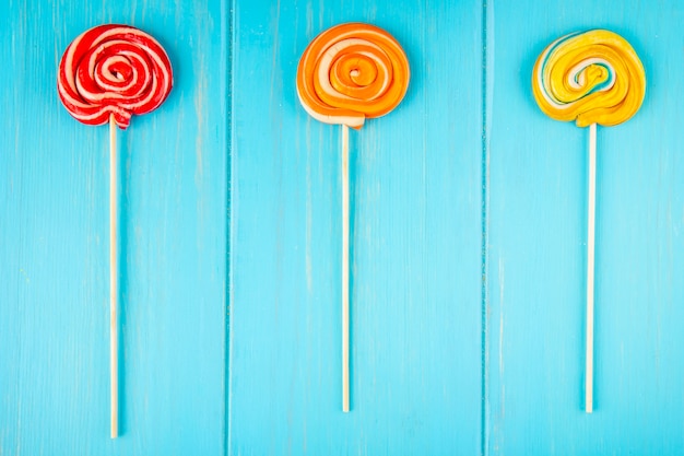 Bovenaanzicht van kleurrijke lollies op een stok op blauwe houten achtergrond