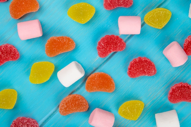Bovenaanzicht van kleurrijke smakelijke marmelade snoepjes en marshmallows verspreid over blauw