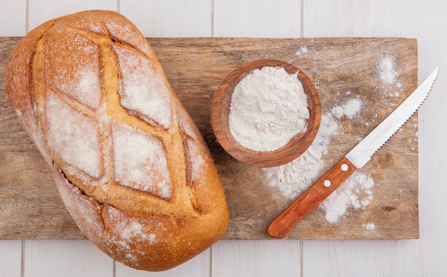 Bovenaanzicht van knapperig brood met kom bloem en mes op snijplank op houten achtergrond