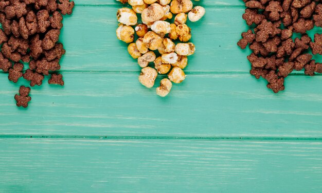 Bovenaanzicht van knapperige chocolade cornflakes en karamel popcorn op groene achtergrond met kopie ruimte