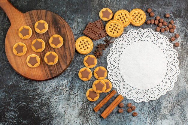 Bovenaanzicht van koekjes op houten schotel met veel snoep en een stuk wit kant op grijze grond