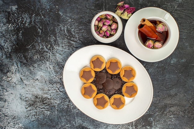 Bovenaanzicht van koekjes op witte plaat met een kopje kruidenthee met een kom met droge bloem op grijze grond