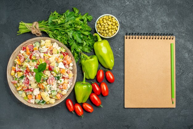 Bovenaanzicht van kom groentesalade met groenten en blocnote aan kant op donkergroene tafel