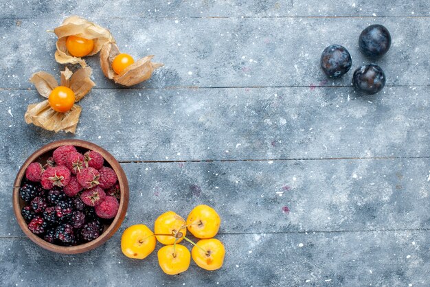 Gratis foto bovenaanzicht van kom met bessen vers rijp fruit op grijs, bessen fruit vers zacht bos