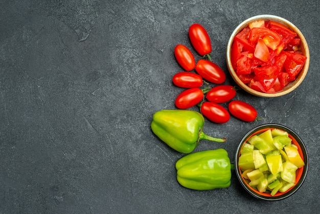 Bovenaanzicht van kommen paprika en tomaten met groenten aan de zijkant en vrije ruimte voor uw tekst op donkergroene achtergrond