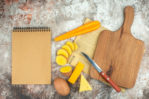 Gratis foto bovenaanzicht van kookachtergrond met verschillende groenten en twee soorten kaasmes en houten snijplank op gemengde kleurachtergrond