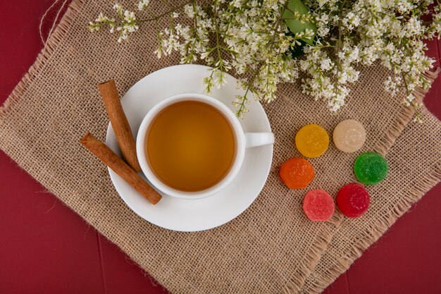 Bovenaanzicht van kopje thee met kaneel gekleurde marmelades en bloemen op een beige servet