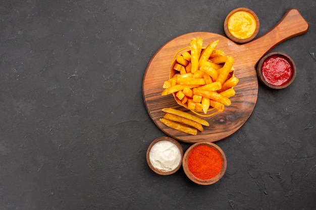 Bovenaanzicht van lekkere frietjes met sauzen op zwart