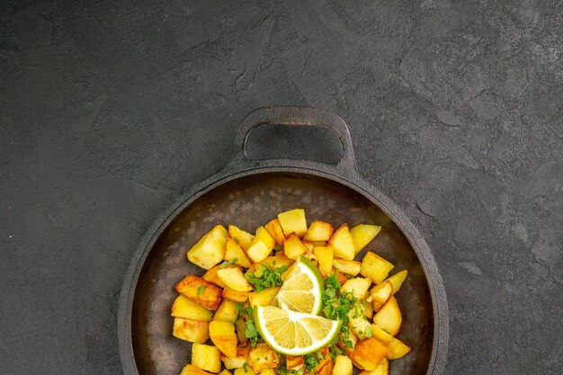 Bovenaanzicht van lekkere gebakken aardappelen in pan met schijfjes citroen op donkere ondergrond