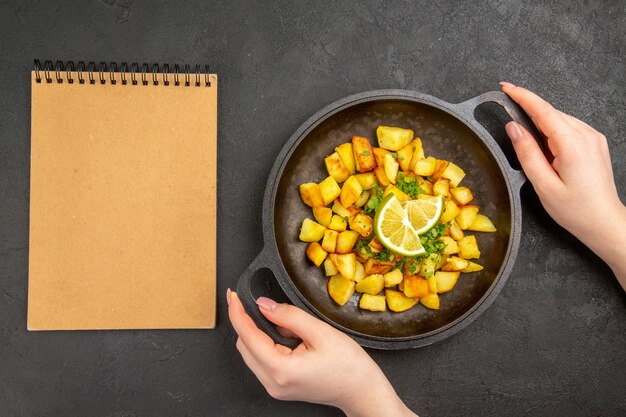 Bovenaanzicht van lekkere gebakken aardappelen in pan met schijfjes citroen op donkere ondergrond