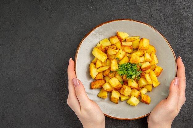 Bovenaanzicht van lekkere gebakken aardappelen in plaat met Groenen op het donkere oppervlak