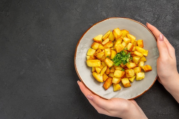 Bovenaanzicht van lekkere gebakken aardappelen in plaat met Groenen op het donkere oppervlak