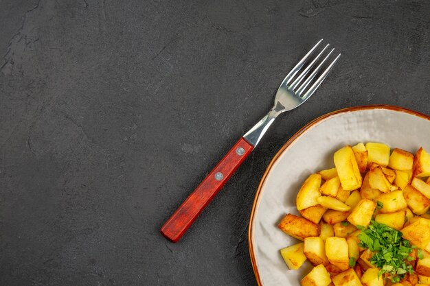 Bovenaanzicht van lekkere gebakken aardappelen in plaat met Groenen op het donkere oppervlak