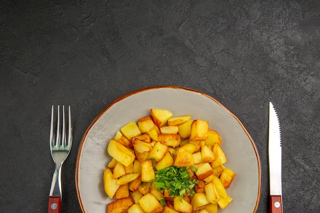 Bovenaanzicht van lekkere gebakken aardappelen in plaat met Groenen op het donkere oppervlak