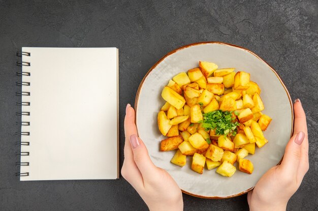 Bovenaanzicht van lekkere gebakken aardappelen in plaat met Groenen op het donkere oppervlak