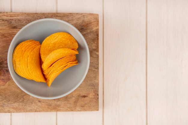 Bovenaanzicht van lekkere knapperige chips op een kom op een houten keukenbord op een beige houten tafel met kopie ruimte