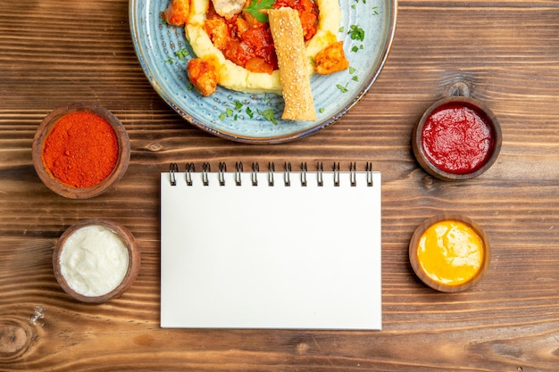 Bovenaanzicht van lekkere plakjes kip met aardappelpuree en kruiderijen op bruine tafel.