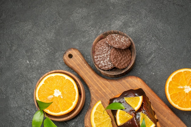 Bovenaanzicht van lekkere taarten gesneden sinaasappelen met koekjes op snijplank op donkere tafel