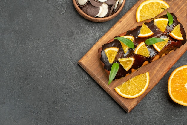 Bovenaanzicht van lekkere taarten gesneden sinaasappelen met koekjes op snijplank op zwarte tafel