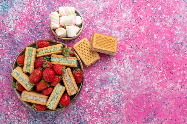 Bovenaanzicht van lekkere wafelkoekjes met marshmallows en verse rode aardbeien op roze oppervlak
