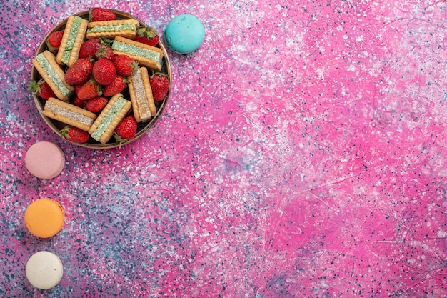 Bovenaanzicht van lekkere wafelkoekjes met verse rode aardbeien en Franse macarons op roze oppervlak