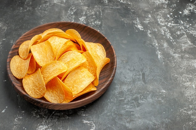 Bovenaanzicht van lekkere zelfgemaakte aardappelchips op een bruine plaat op grijze achtergrond