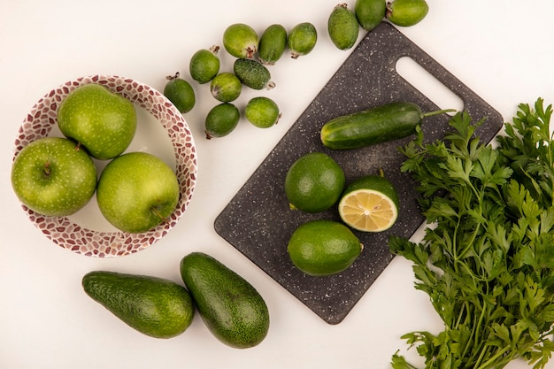 Bovenaanzicht van limoenen op een keukenbord met appels op een kom met komkommer feijoas en avocado's geïsoleerd op een witte muur