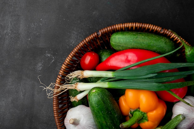 Bovenaanzicht van mand vol groenten als lente-ui peper komkommer en anderen op rechterkant en zwarte ondergrond