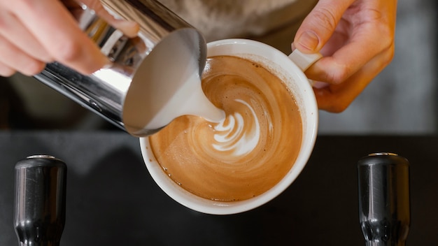 Bovenaanzicht van mannelijke barista melk gieten in koffiekopjes